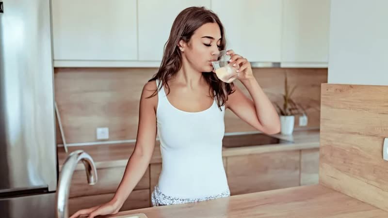 Woman drinking water in a bright kitchen