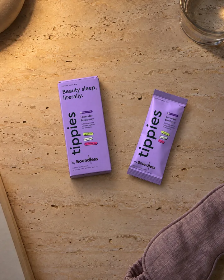 A lavender tippies Beauty + Sleep box and stick on a travertine bedside table with a sleep mask