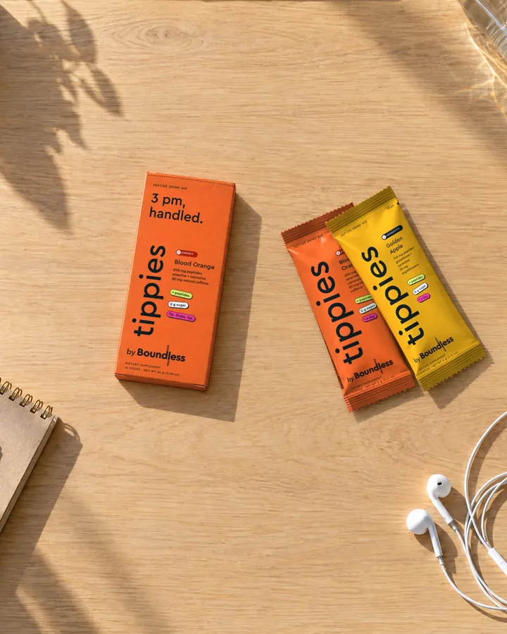 A blood orange tippies Energy box and sticks on a wooden desk with earphones and a notebook