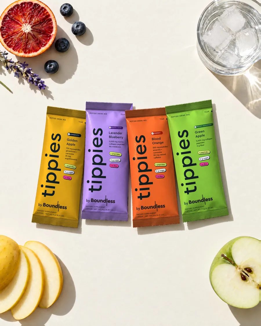 Four tippies by Boundless drink mix sticks laid out with golden apple, blueberries, lavender, blood orange and a glass of iced water